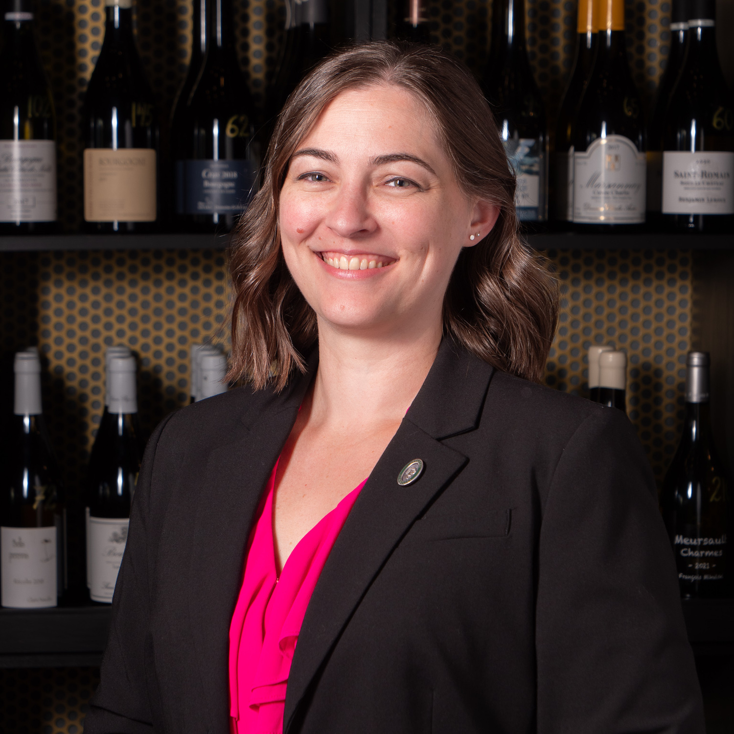 Woman in black blazer and pink shirt smiles at the camera