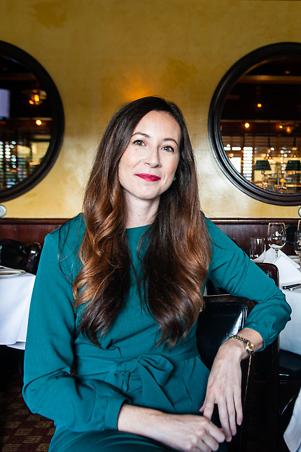 Woman in teal dress sits in restaurant and looks at camera