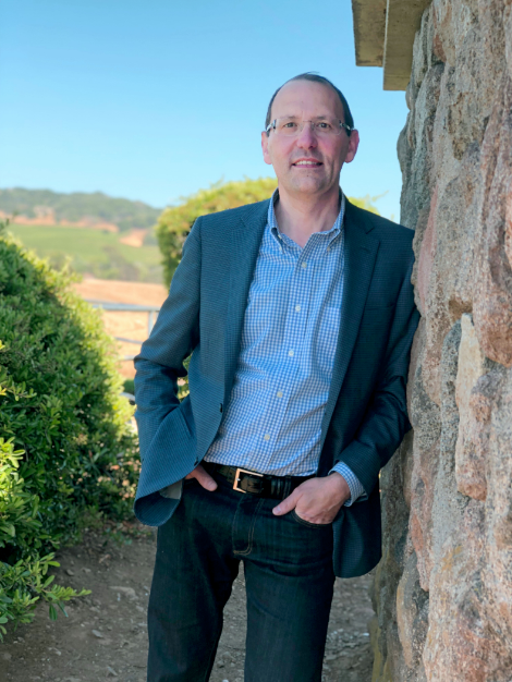 Man in blazer leans against building with landscape in the background