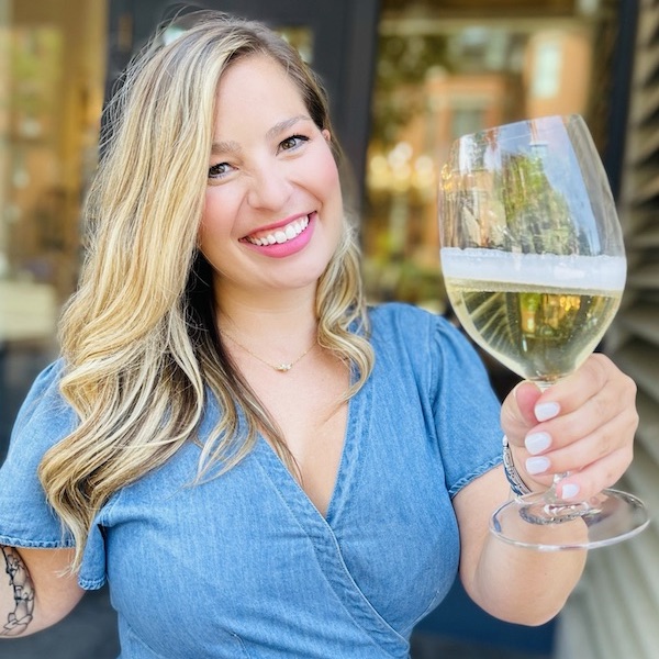 Woman in blue denim dress holding wine glass up toward camera