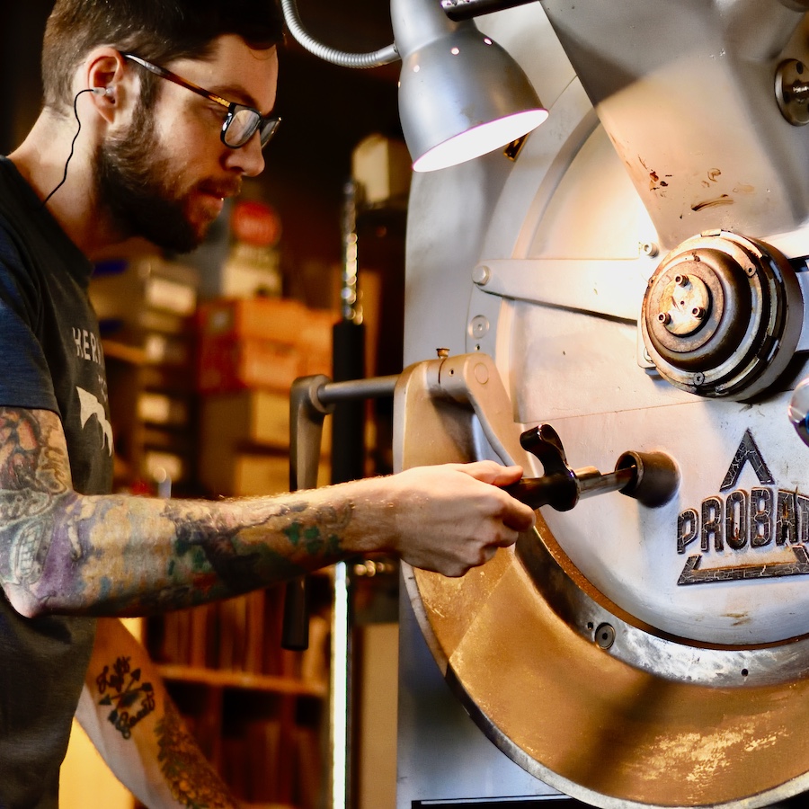 Man with dark glasses operates a large coffee roaster