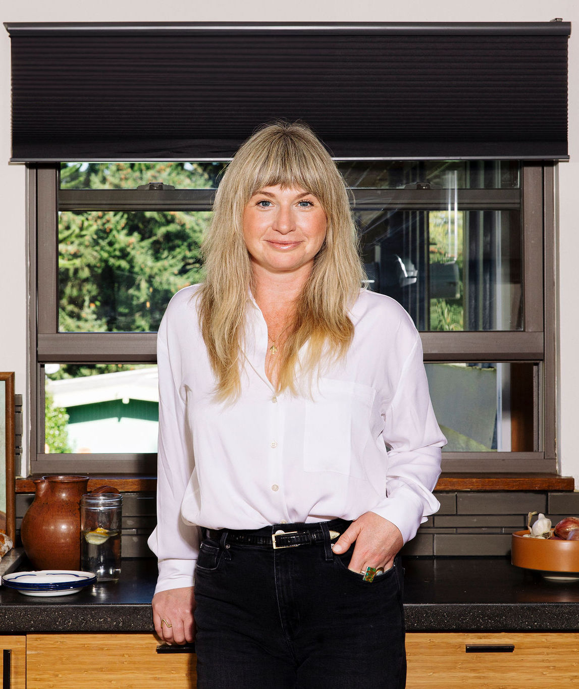 Woman in white shirt stands by counter and smiles at the camera
