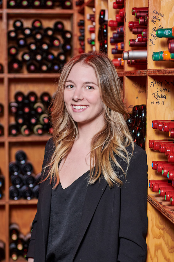 Woman in dark blazer standing in wine cellar smiles at the camera