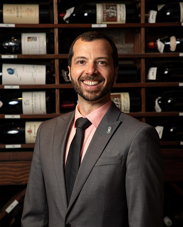Man in suit standing in front of wine storage smiles at the camera