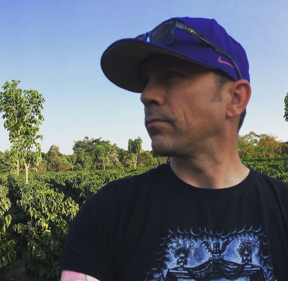 Man in baseball hat looks to the side with green landscape behind him