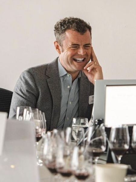 Man laughs while looking at laptop with glasses of wine in the foreground