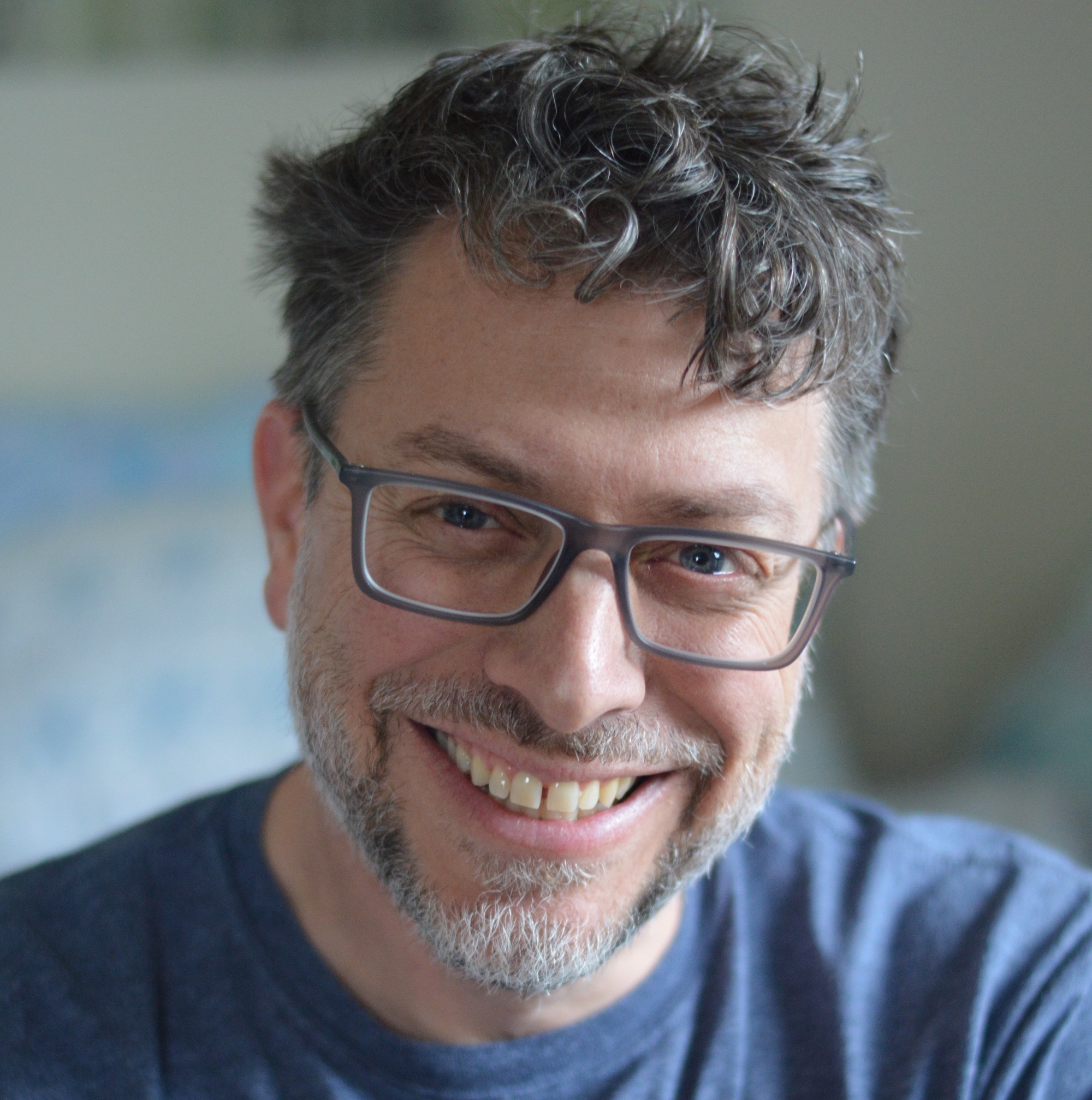 Man with glasses in blue shirt smiles at the camera