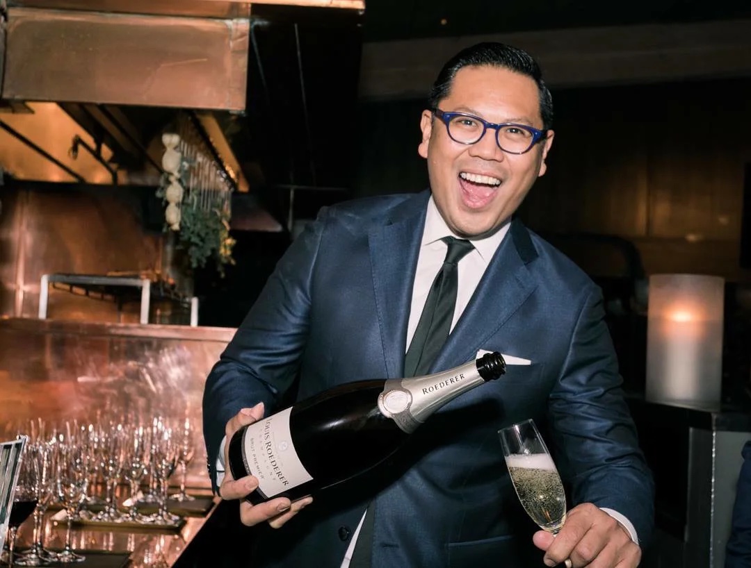 man pouring bottle of wine smiles at camera