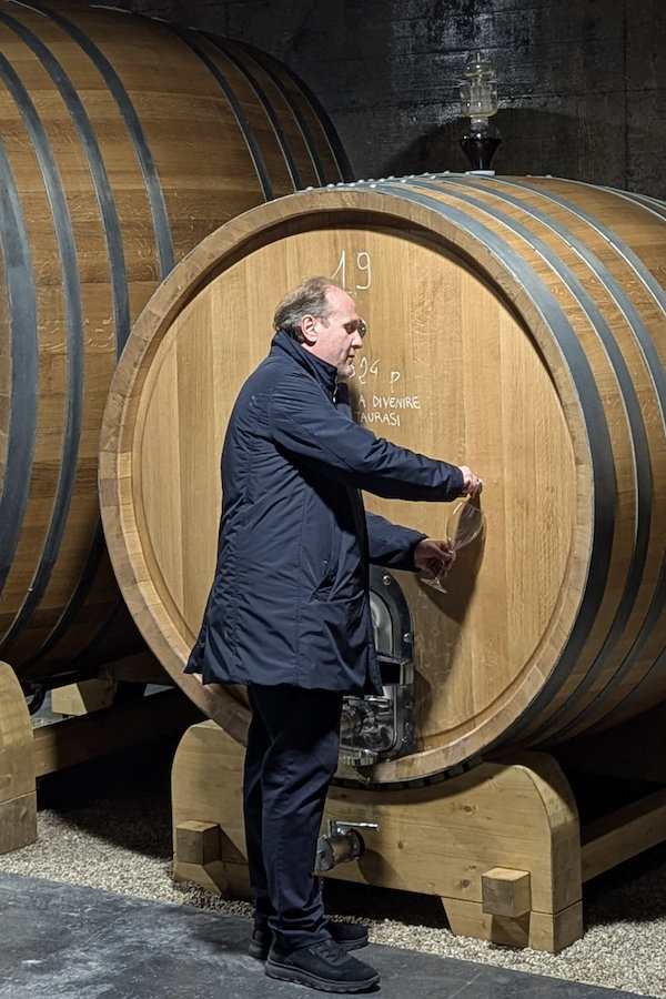 Man in dark coat fills wine glass from barrel