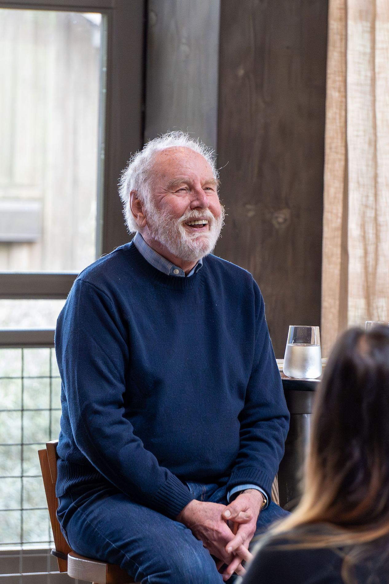 Man in blue sweater sitting on stool smiles