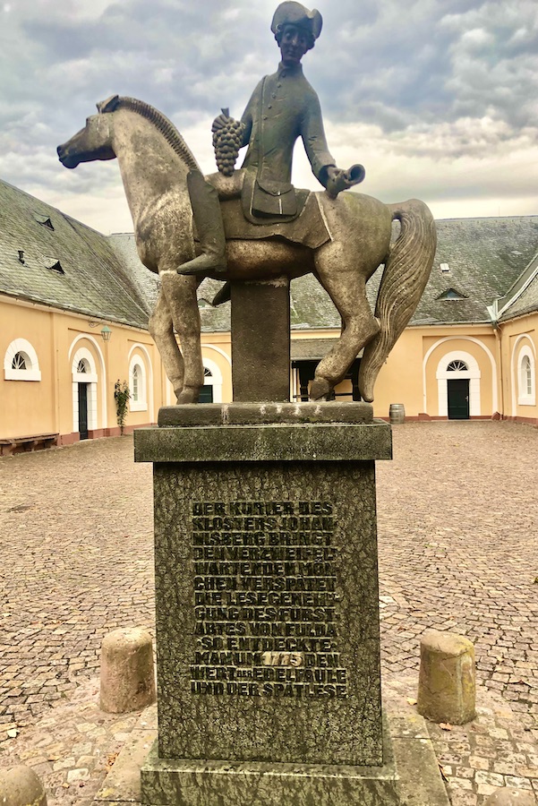 Bronze-colored statue of rider on horse in plaza surrounded by orange buildings