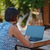 Woman sits at table outside with laptop