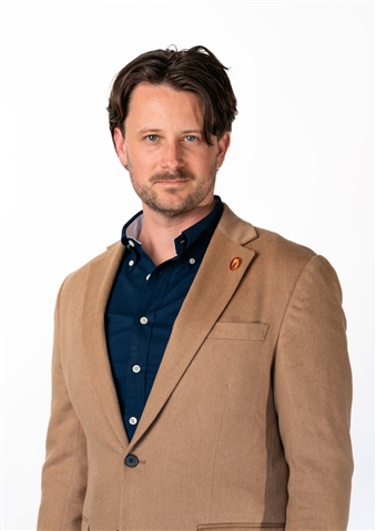 Man in suit jacket looks at camera with white background