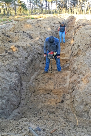 Workers dig deep under the ground in a wide trench