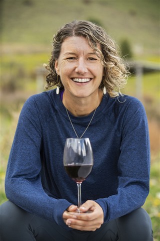 Woman with brown curly hair looks at camera, holding glass of red wine