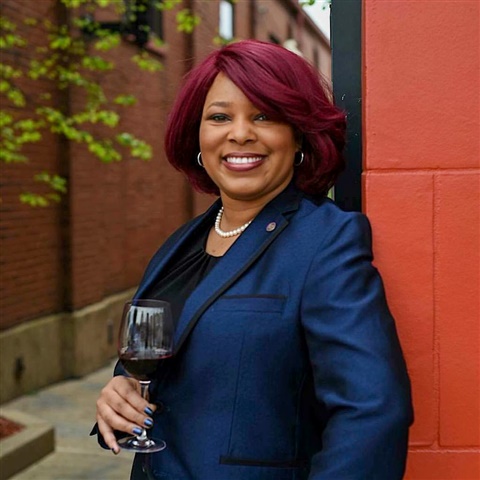 Woman in blue blazer holding a glass of wine smiles at the camera